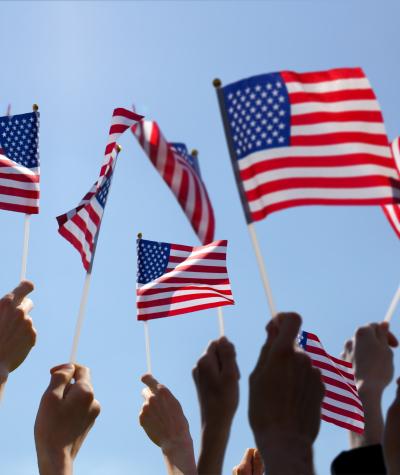 Group of People Waving American Flags over blue sky. Adobe Stock image.