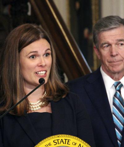 A woman speaking at a podium with a man standing behind her
