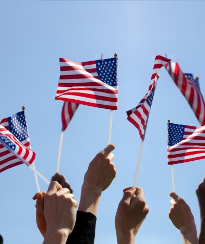 Group of People Waving American Flags over blue sky. Adobe Stock image.