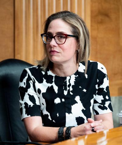 Kyrsten Sinema sitting at a desk looking sideways at the camera