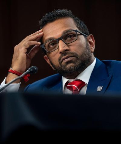 Kash Patel sitting at a desk with his hand raised to his forehead