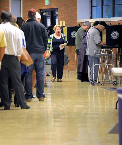 A long line of people waiting to vote, a few people standing at voting booths and a woman walking back down the line.