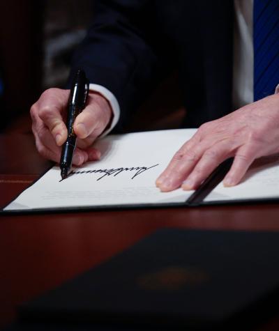 A man's hand signing a piece of paper on a desk