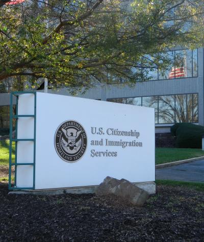 A sign with the Department of Homeland Security seal and the word U.S. Citizenship and Immigration Services in front of an office building