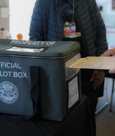 A person inserting a ballot into a box labeled "Official Ballot Box"