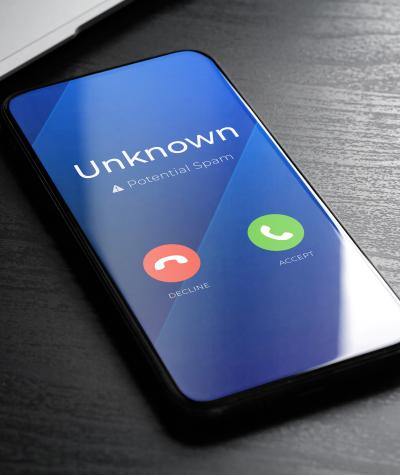 A smartphone on a desk with the words "Unknown, Potential Spam" on the screen and green and red buttons to decline or accept the call.