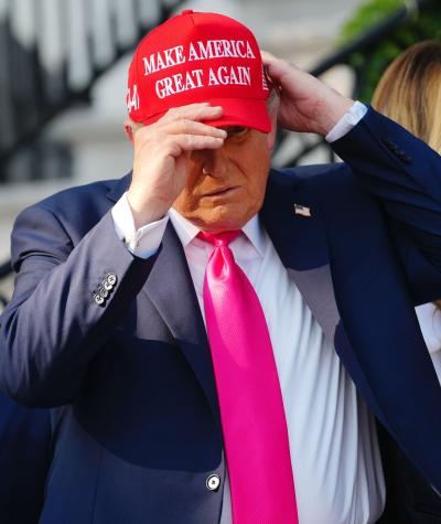 Donald Trump putting on a red had with the words "Make America Great Again" on it.