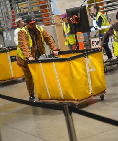 People move large yellow bins full of ballots