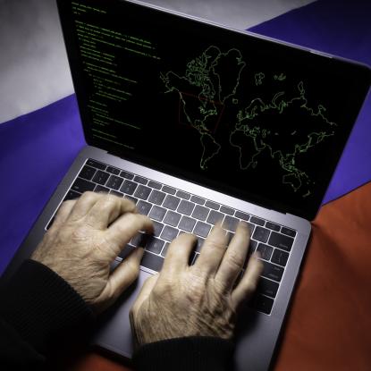 Man typing on laptop with map of United States and Russian flag in background