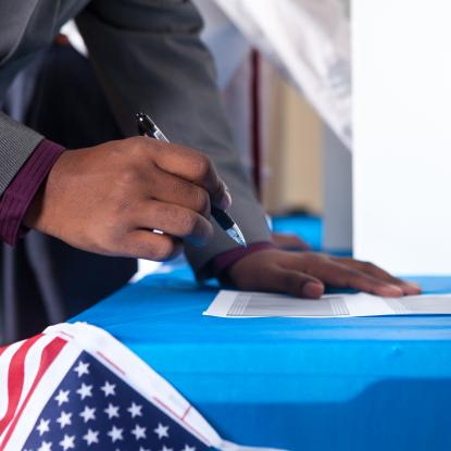 Man's hands writing on ballot in voting booth