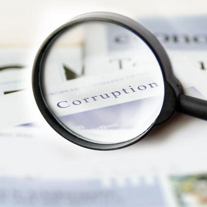 A magnifying glass highlighting the word "corruption" in a newspaper.
