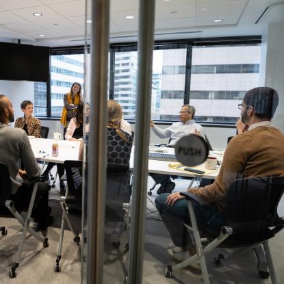 People sit around a table in a conference room seen through an open glass door