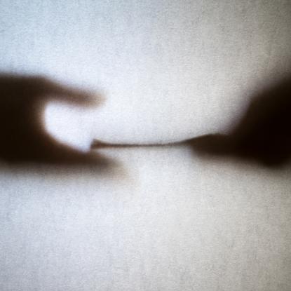 Two hands seen through frosted glass. One is passing a stack of what looks like money to another.