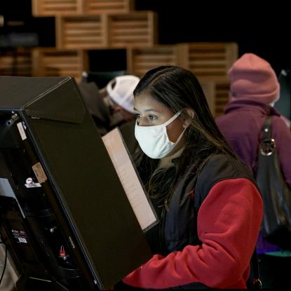 Two women wearing masks use voting machines