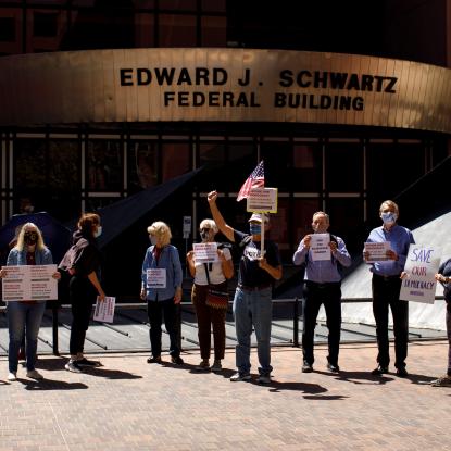 People gathered on a sidewalk holding signs that say "#ForthePeopleAct" and "Save Our Democracy"