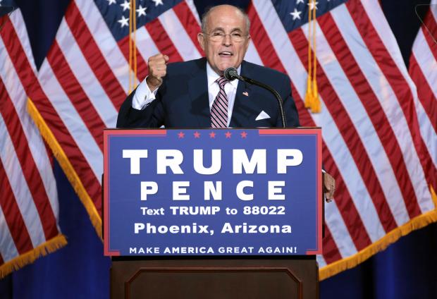 Rudy Giuliani speaking at a podium with a Trump/Pence sign on the front