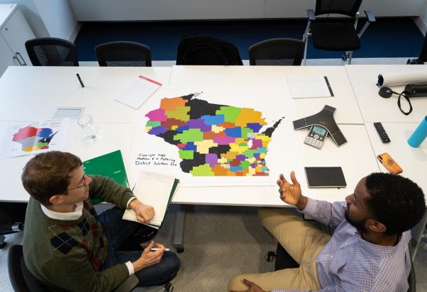 A top down view of a map of Wisconsin on a table with two people sitting next to it having a discussion