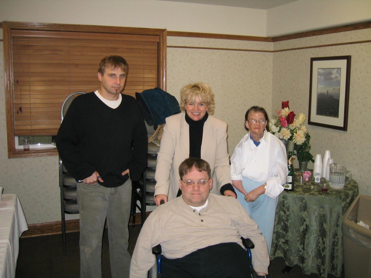 Four people posing for a photo, three standing and one in a wheelchair
