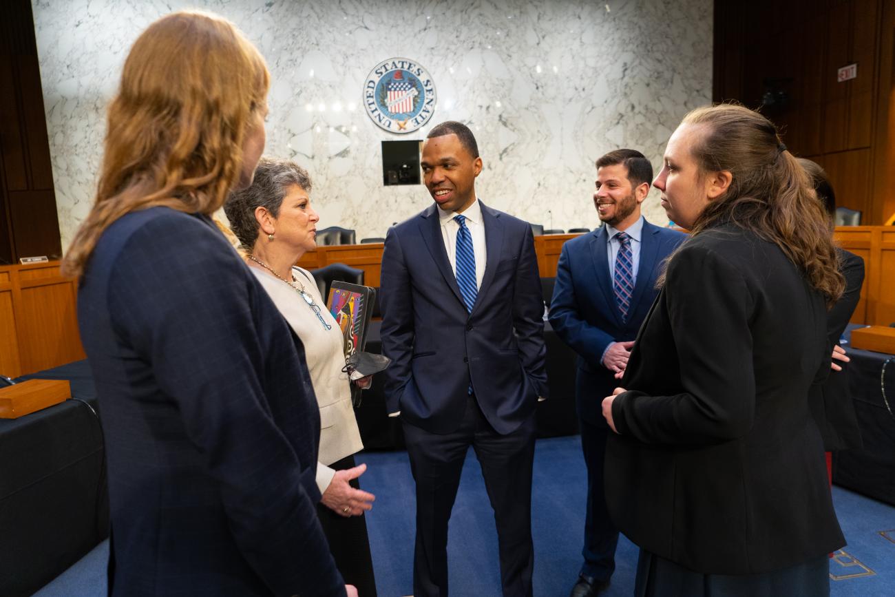 A group of people standing in a Senate committee room