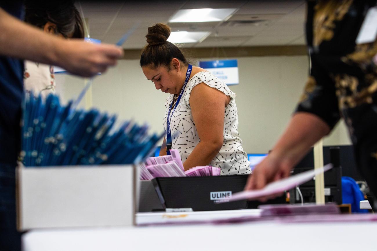 A woman bends over a table with boxes of ballots