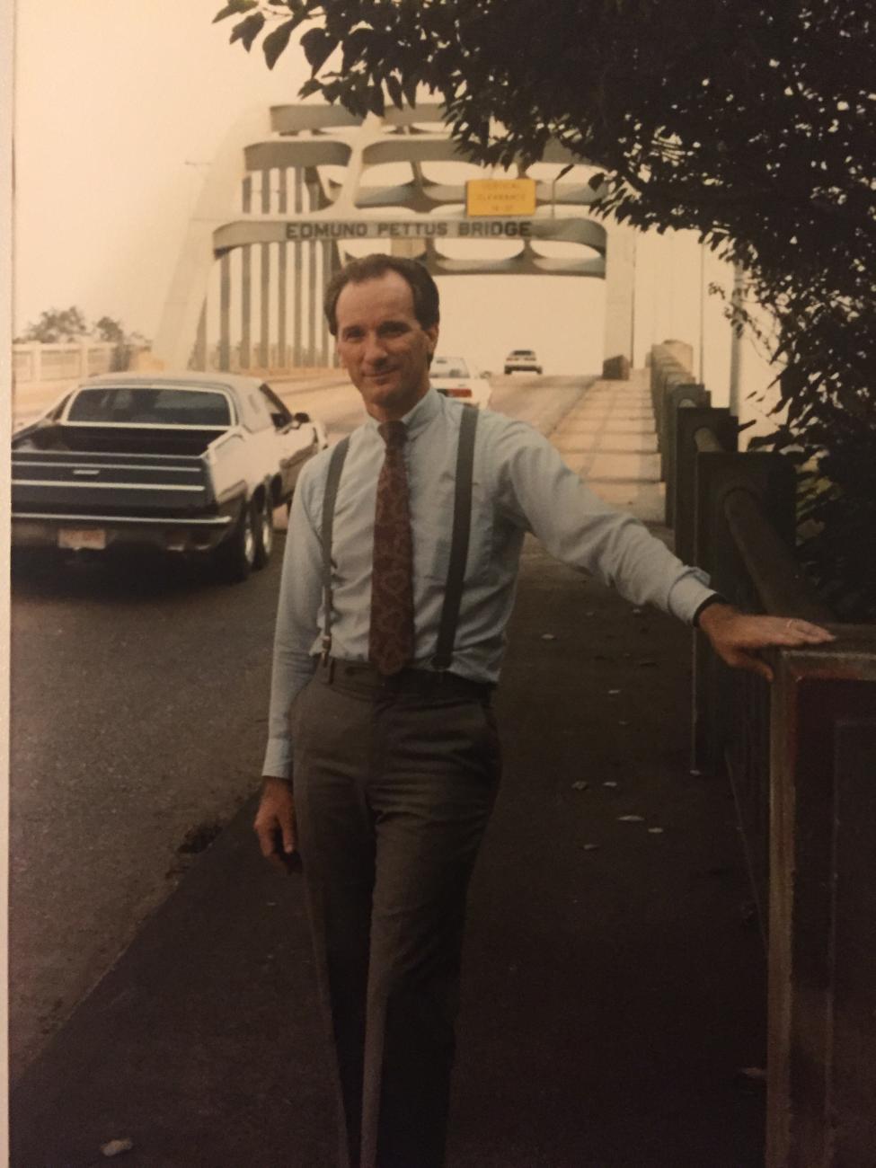 Gerry Hebert posing in front of a bridge with a car in the background